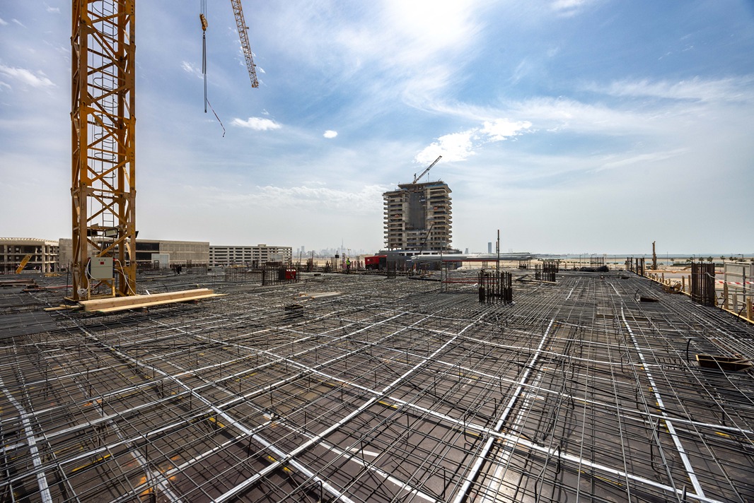 Beach Walk Iii By Imtiaz Construction site featuring a crane, exposed steel rebar, and a partially completed building under a blue sky.